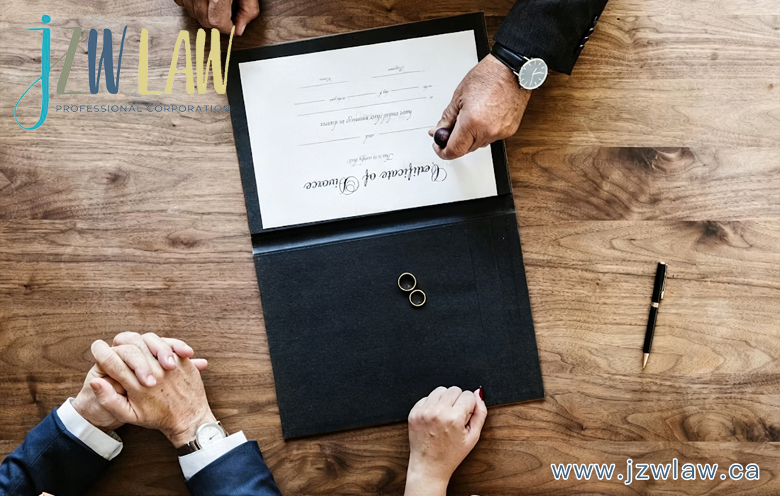 Top-down view of a contract being stamped on a wooden desk, with two people clasping hands nearby and rings inside an open folder (law firm branding visible).