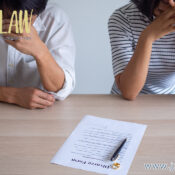 Two people sit at a table with a divorce form and pen, appearing stressed as they review the paperwork.
