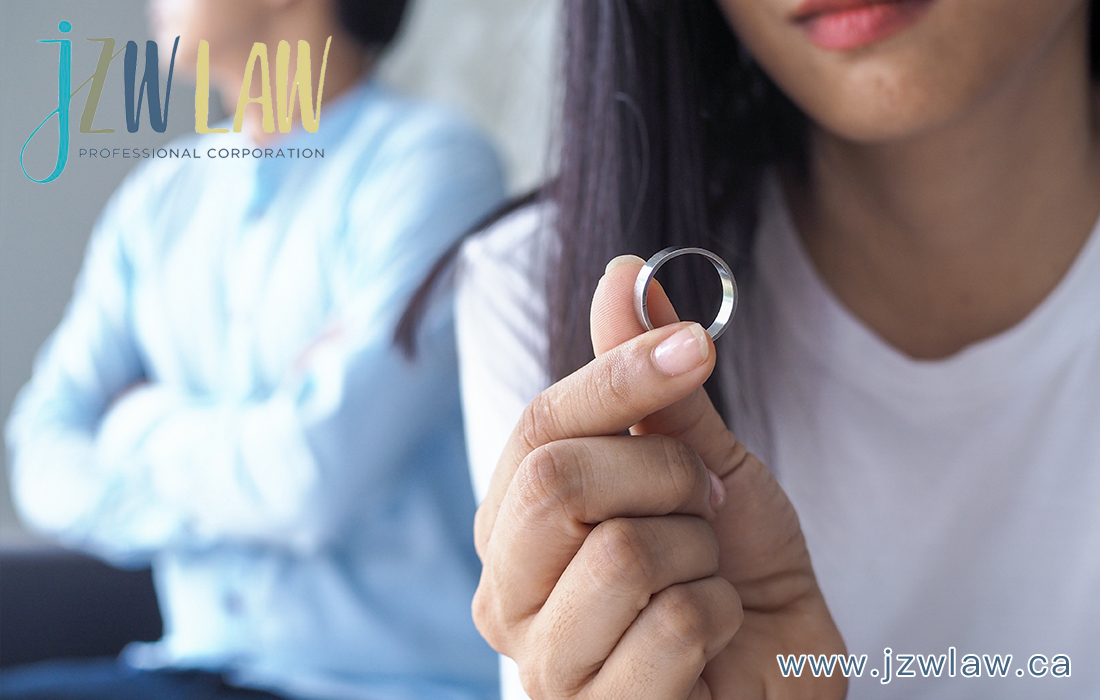 Close-up of a hand holding a silver ring, with a blurred person in the background and the jzwLAW professional corporation logo in the corner.