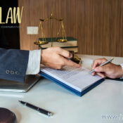 Two professionals sign a legal document at a desk, with a gavel, scales of justice, and a laptop nearby; jzwLAW branding visible in the corner.