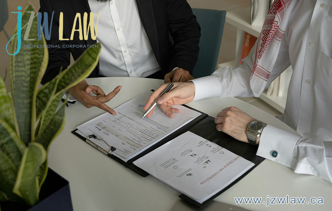 Two professionals sign and discuss documents at a white table in a law office, with a pen over a contract open in a binder.