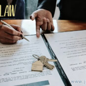 Two people sign legal documents on a wooden table with a house key and keychain resting on the pages.