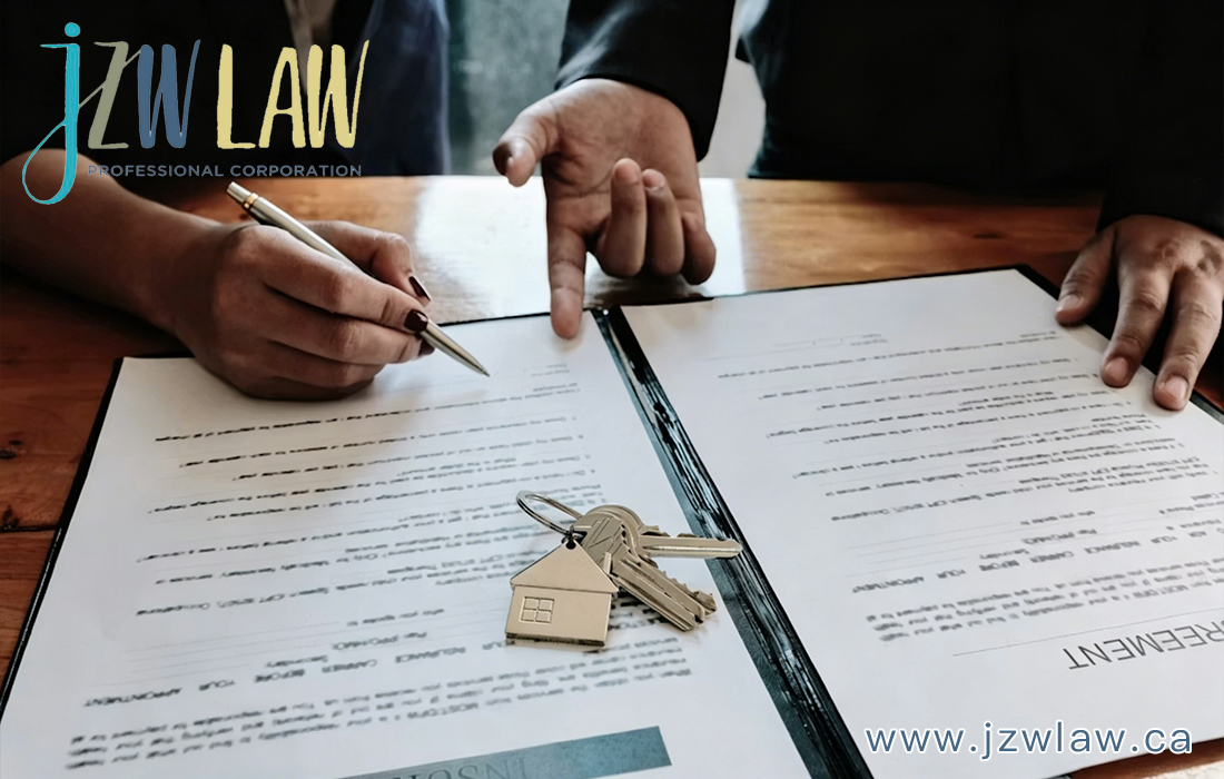 Two people sign legal documents on a wooden table with a house key and keychain resting on the pages.