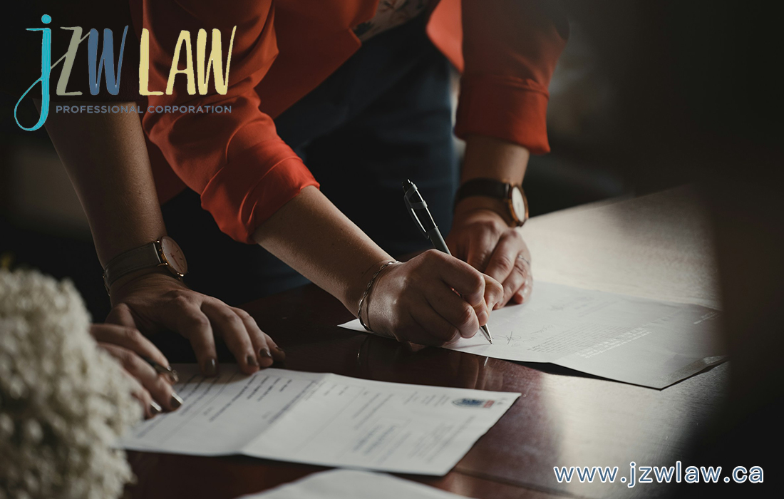 Hands signing documents on a wooden table, law firm branding visible in the corner.