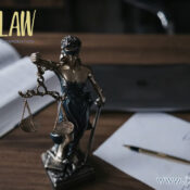 Statue of Lady Justice holding scales on a wooden desk, with an open book, a tablet, and legal documents; jzwLAW Professional Corporation logo in the corner.