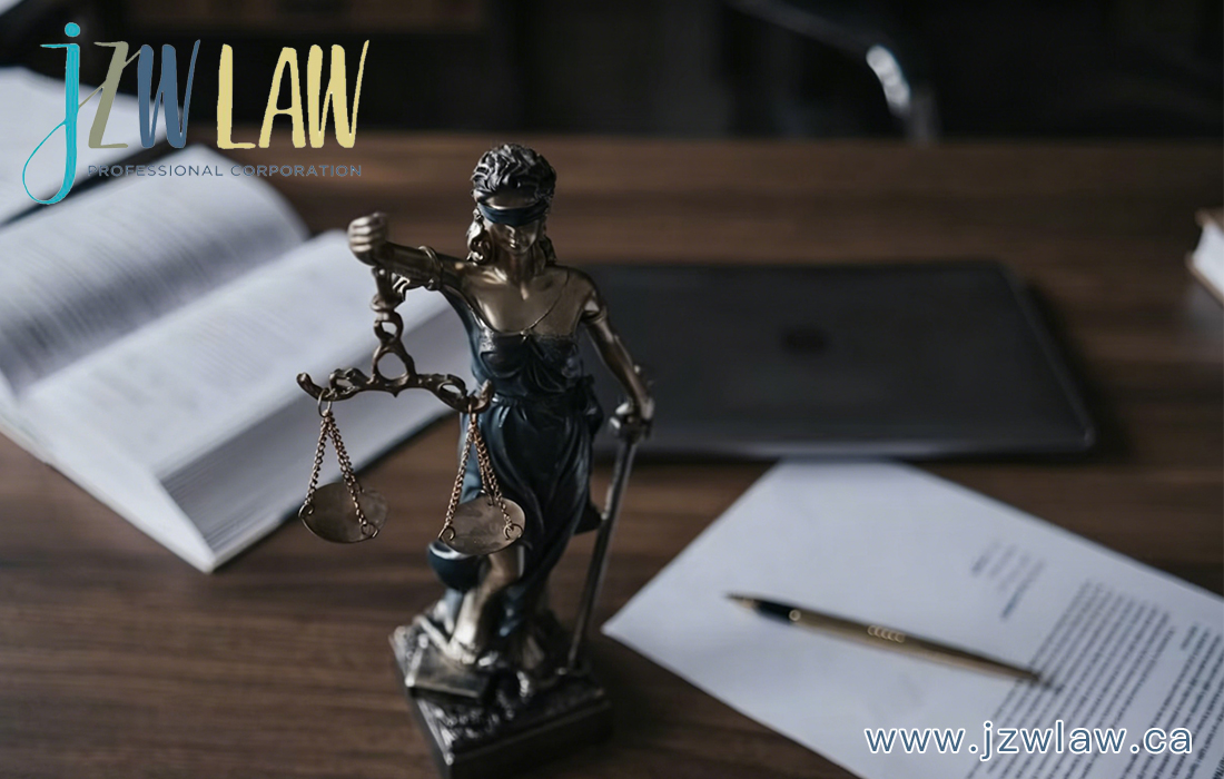Statue of Lady Justice holding scales on a wooden desk, with an open book, a tablet, and legal documents; jzwLAW Professional Corporation logo in the corner.
