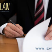 Person in a suit signing documents at a wooden desk; law firm logo in the top-left and www.jzwlaw.ca in the bottom-right.